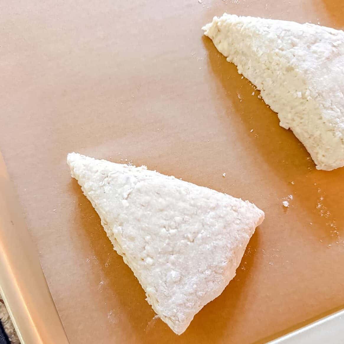 Unbaked triangular Colonial Scones dough on a parchment-lined baking sheet, ready to evoke the flavors of an Early American Recipe perfect for your tea table.