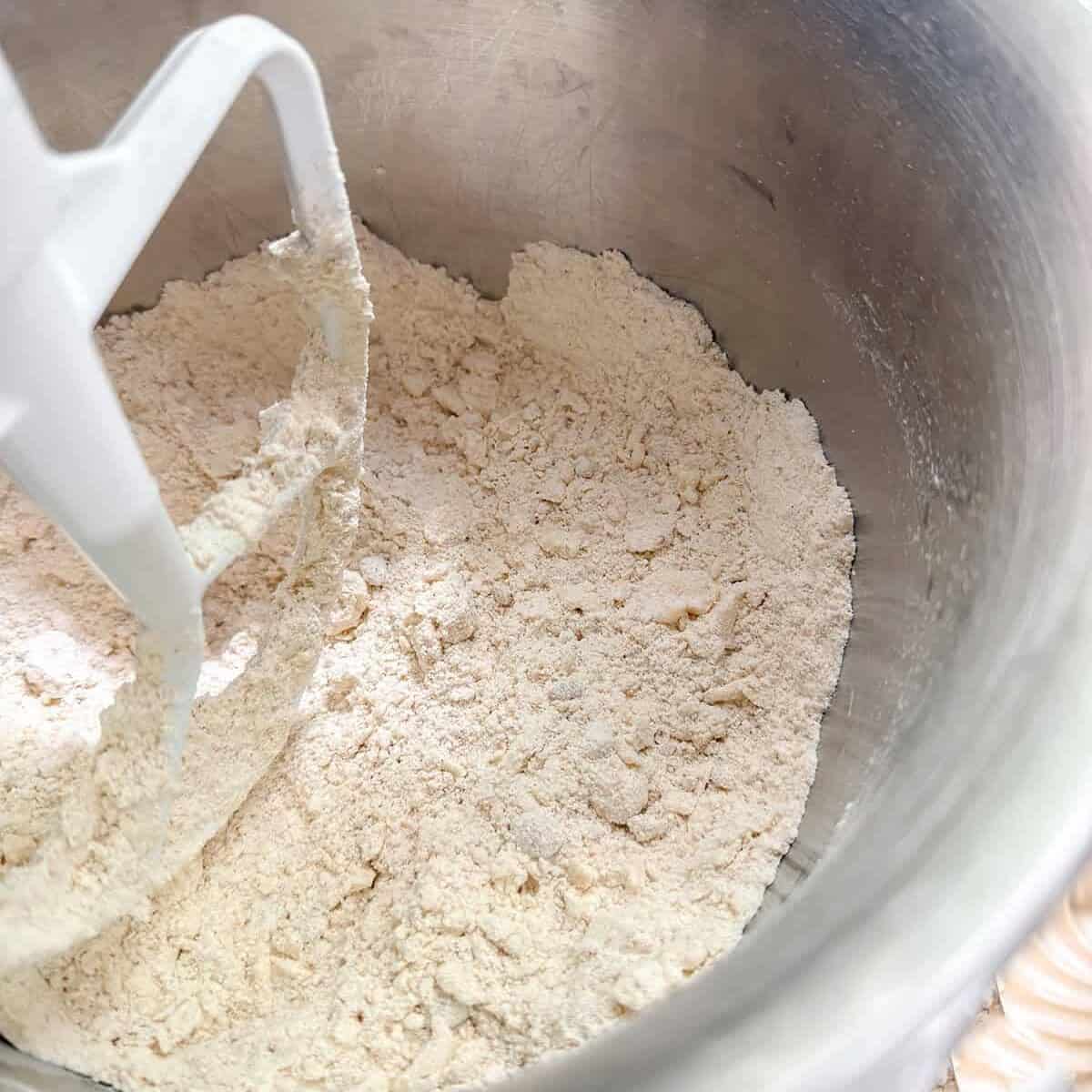 A metal mixing bowl with flour and a paddle attachment, showing the early stage of mixing dry baking ingredients for Colonial Scones that might have graced an Early American tea table.