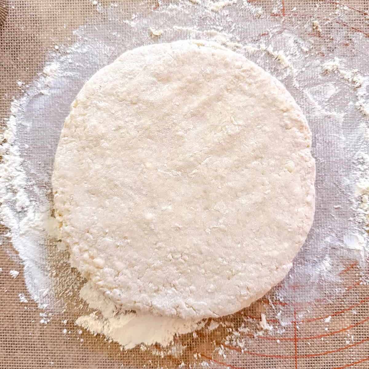 A round disc of dough rests on a floured surface with a baking mat featuring red measurement markings, ready to be shaped into Colonial Scones-a nod to an Early American recipe perfect for the tea table.