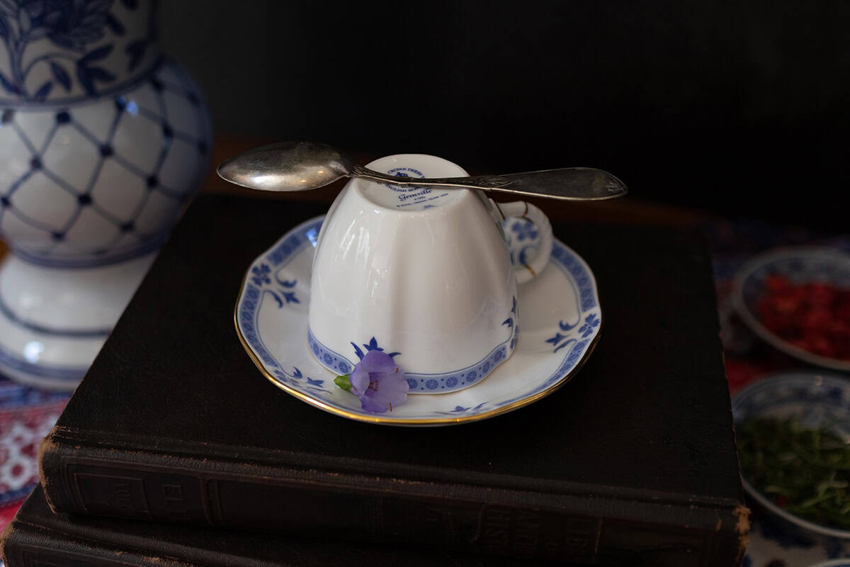 A teacup placed upside down on a saucer with a spoon resting on top, a small purple flower beside it, and a stack of books beneath to signal that no British tea would be served with the statement, "I shall take no tea."