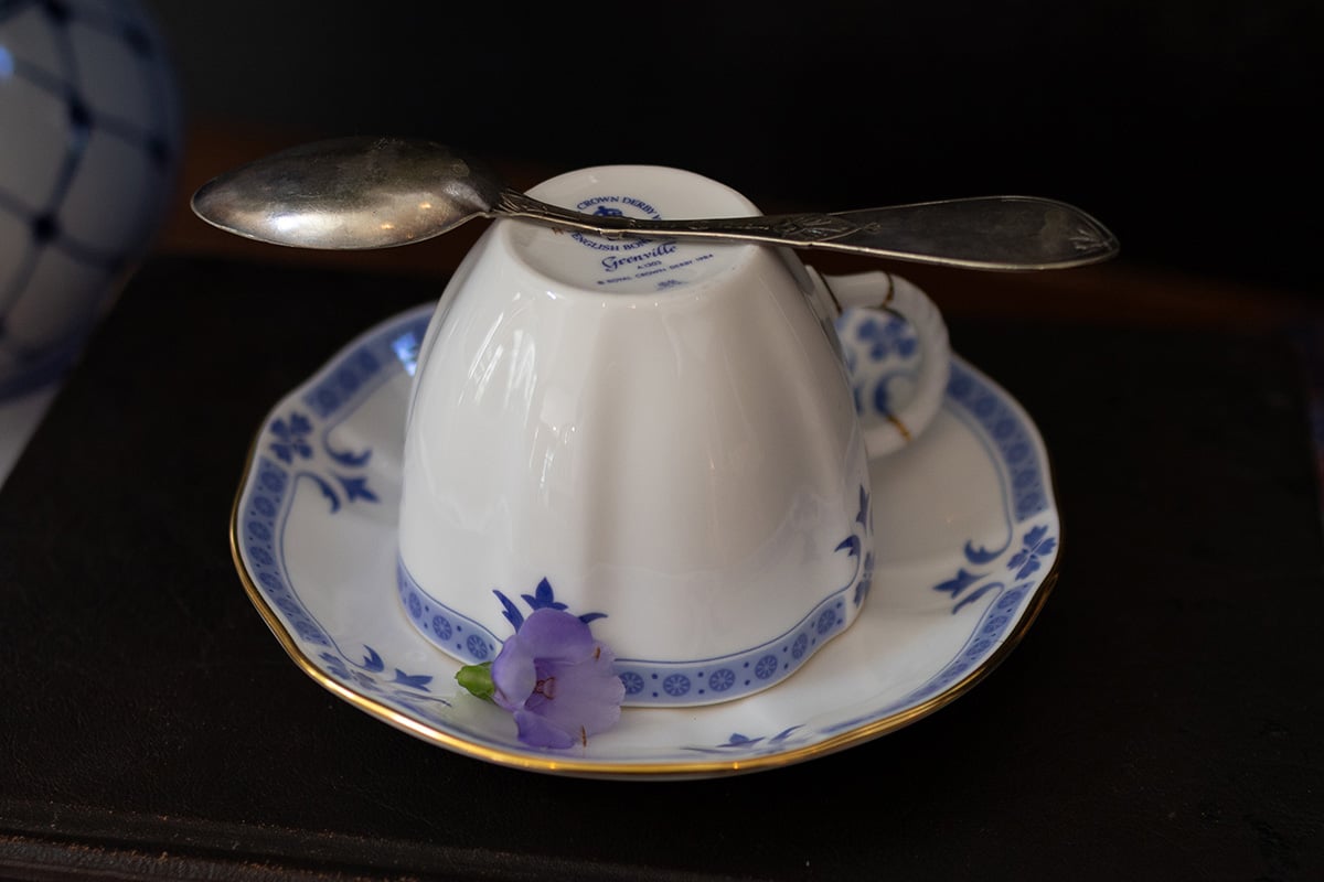 An upside-down teacup on a saucer with a silver spoon rests on top, accompanied by a small purple flower-an elegant nod to the classic Liberty Tea recipe tradition.