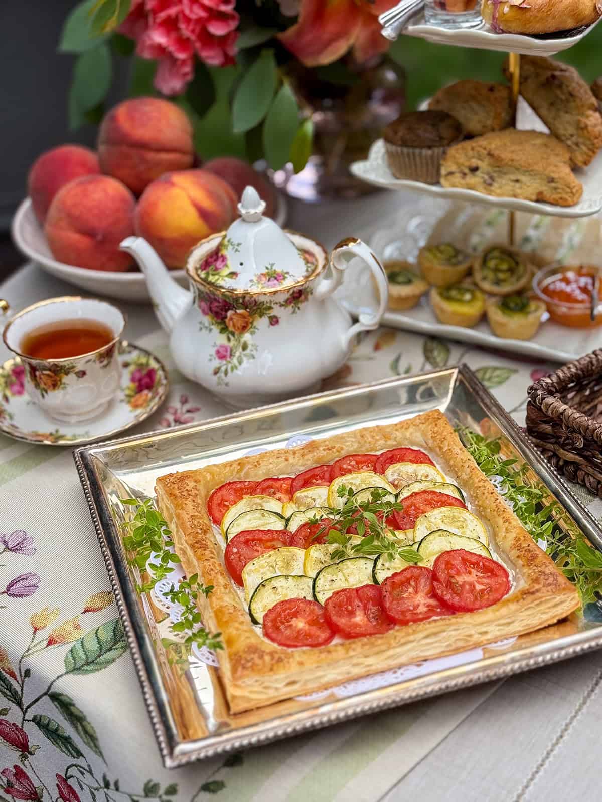 A puff pastry tian provencal tart topped with sliced tomatoes and zucchini rests on a silver tray.