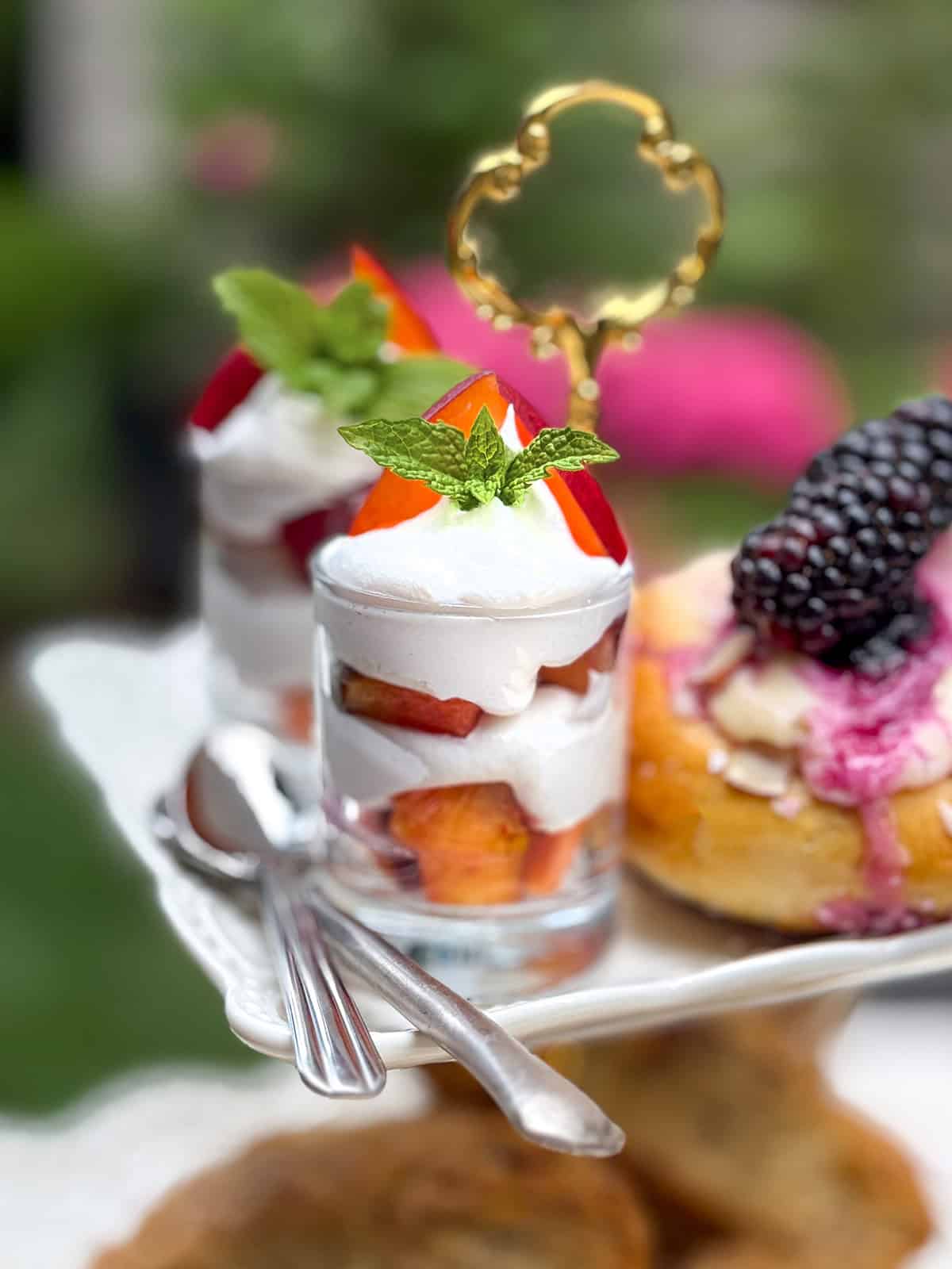 Two glass parfaits layered with Chantilly cream, fresh peach, and garnished with mint, are placed on a 3-tier tray.
