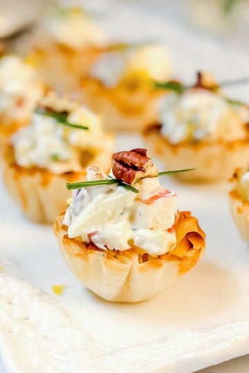 Mini phyllo tartlets filled with a creamy apple Gorgonzola filling, garnished with chopped herbs and pecans.