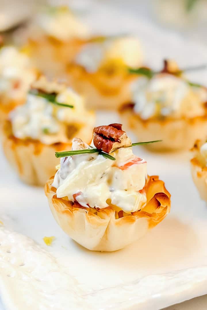 Mini phyllo tartlets filled with a creamy apple Gorgonzola filling, garnished with chopped herbs and pecans.