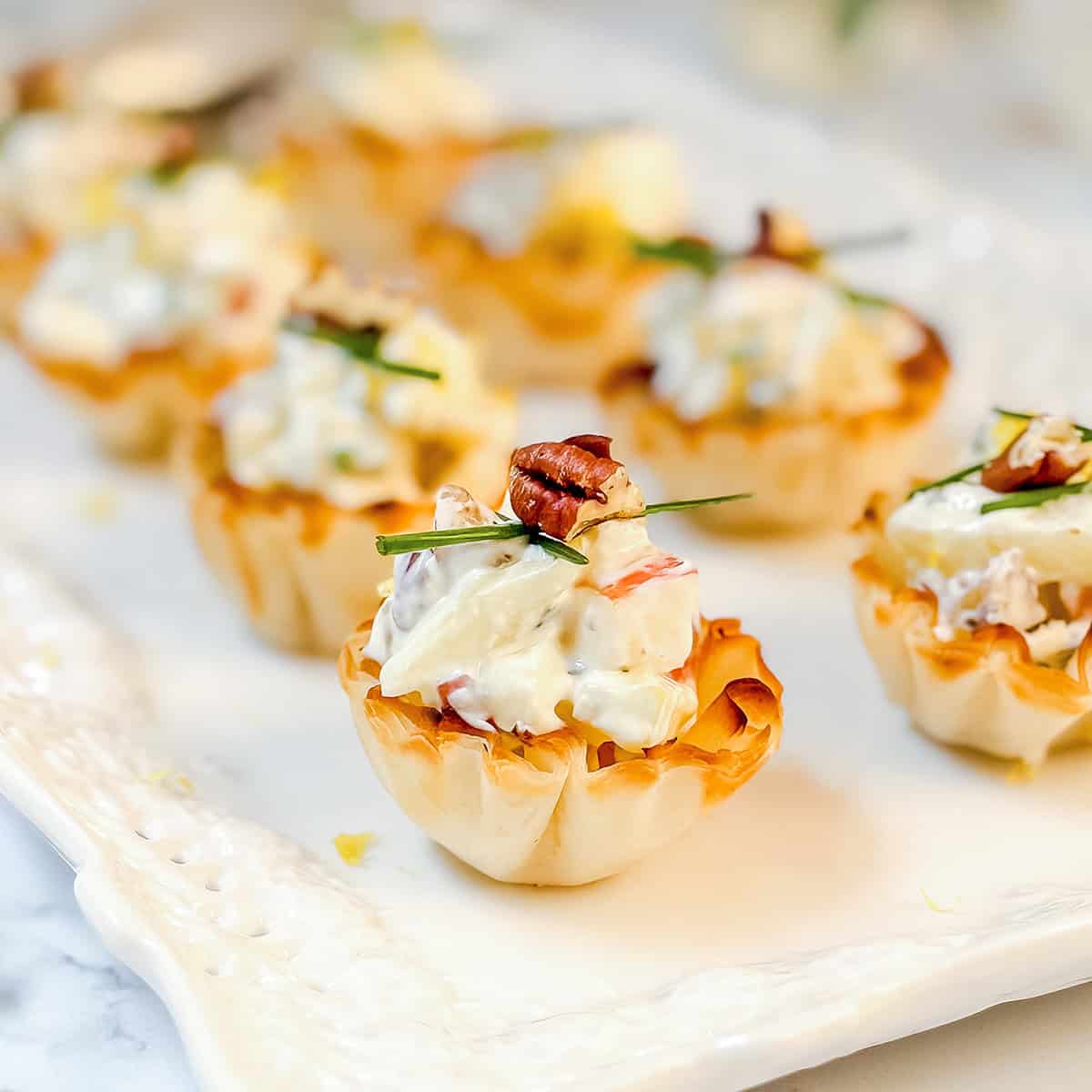 Mini phyllo tartlets filled with a creamy apple Gorgonzola filling, garnished with chopped herbs and pecans.