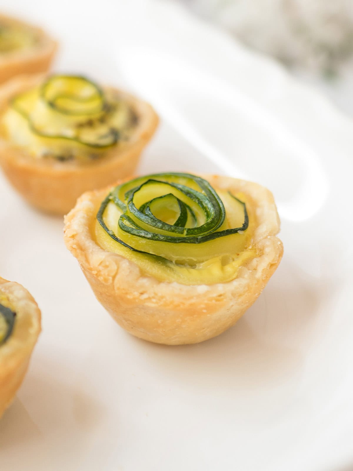 Mini zucchini rose quiche with feta in a flaky pastry shell on a white plate.