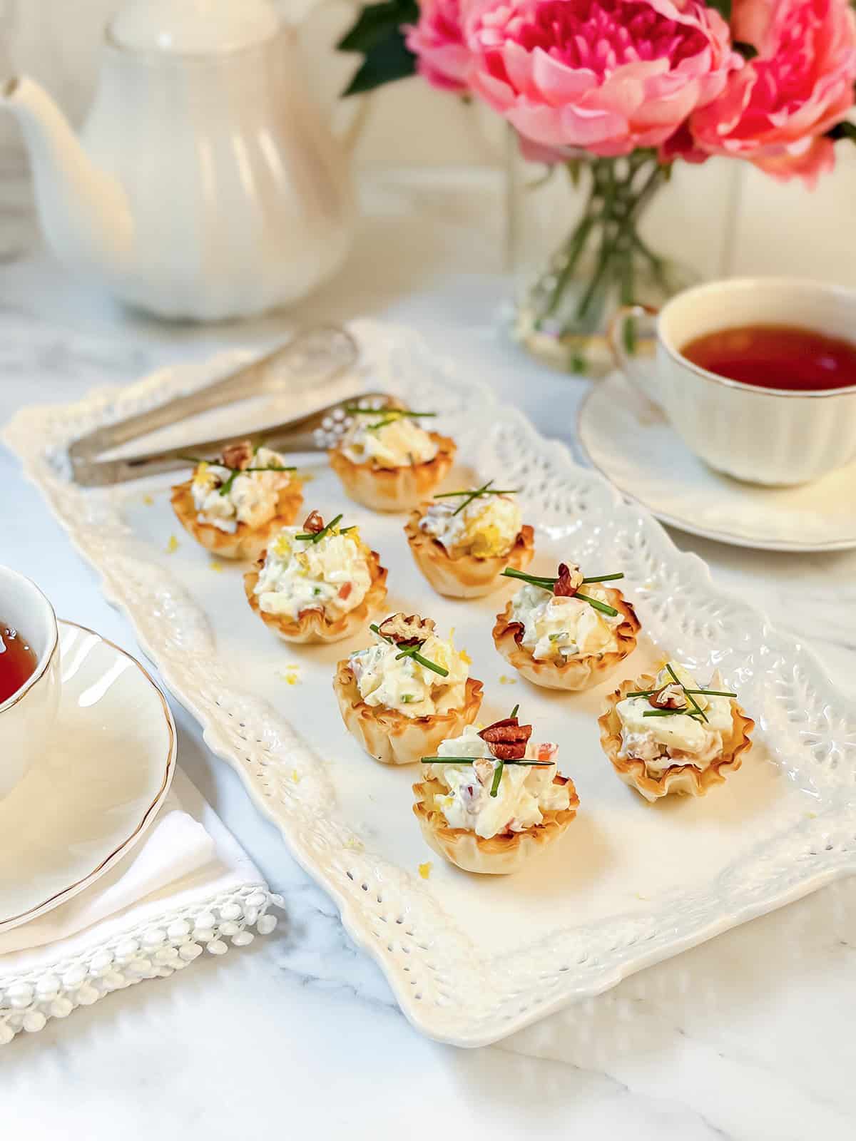 A rectangular tray with mini phyllo tartlets filled with a creamy apple filling, garnished with herbs.
