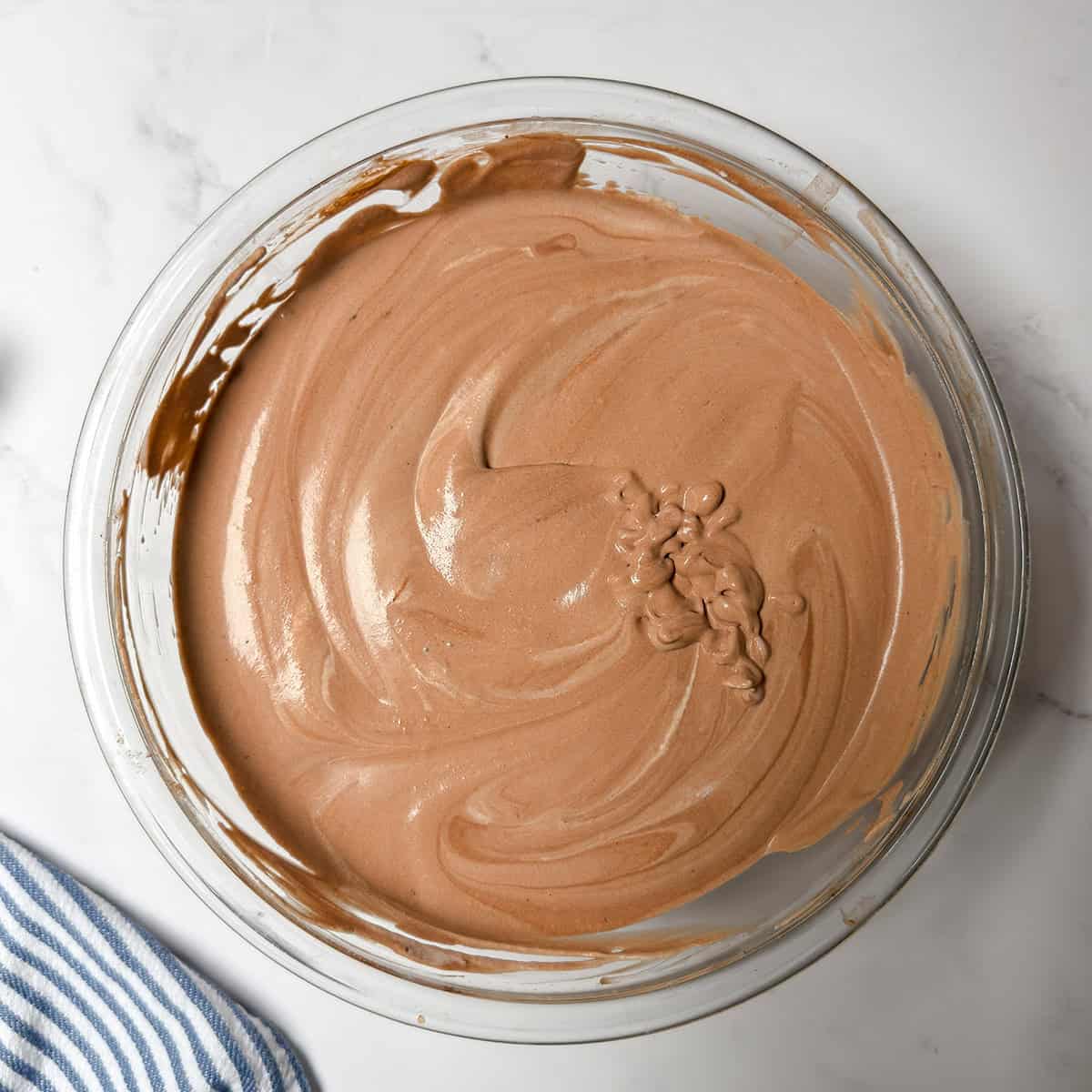 Whipped cream folded into the chocolate condensed milk mixture in a glass bowl.