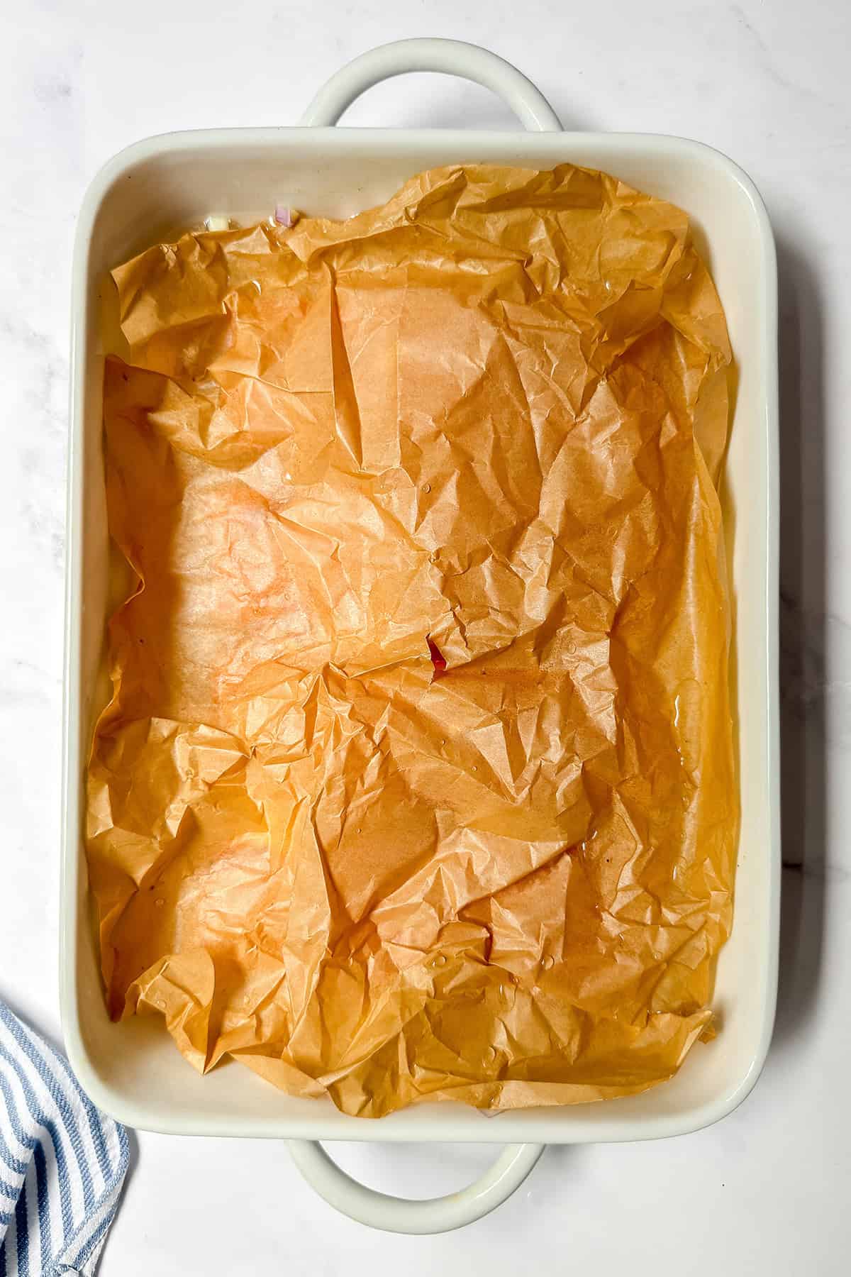 A rectangular white baking dish covered with a sheet of crumpled brown parchment paper, perfect for baking Salmon in a rich Herb Cream Sauce.