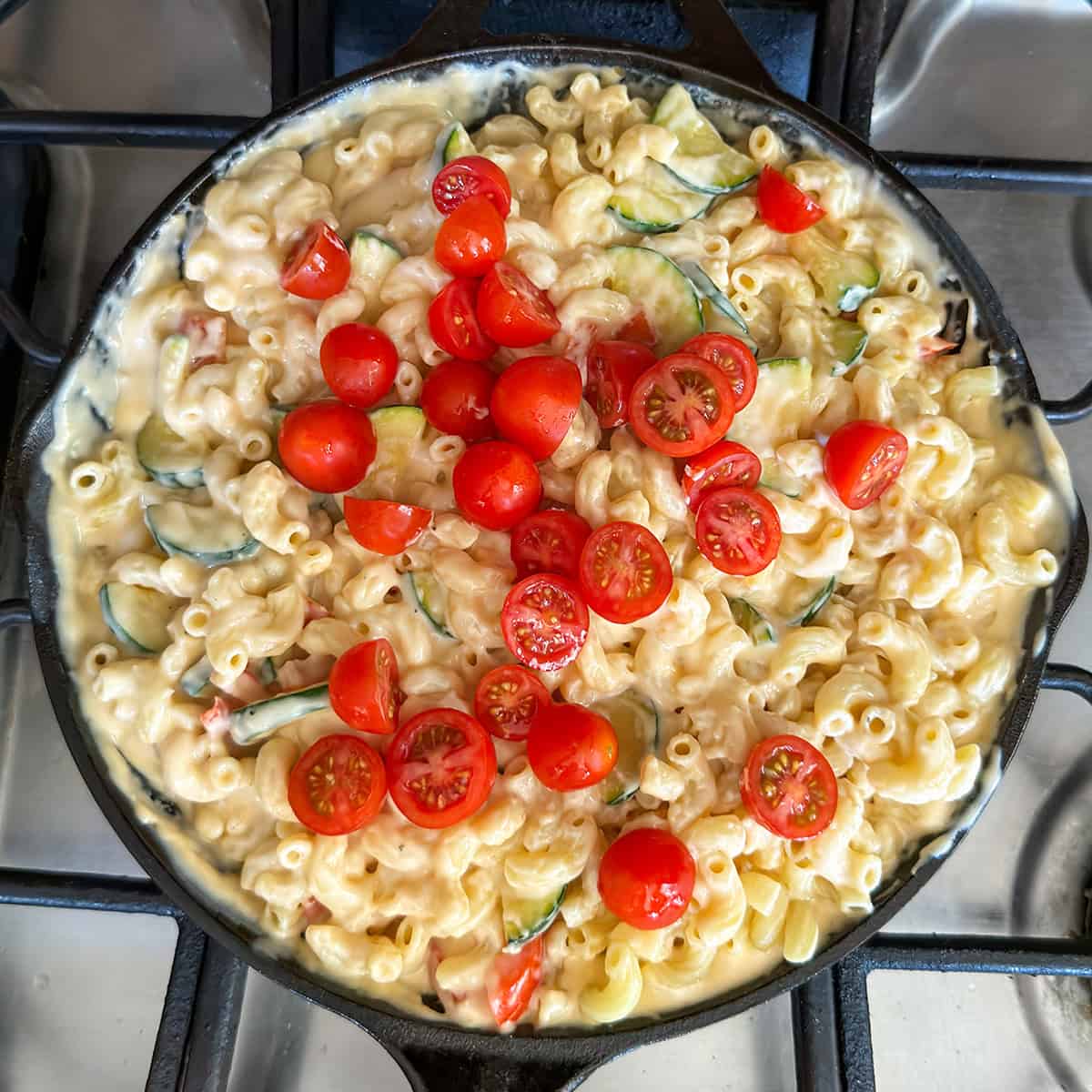 A skillet of creamy Skillet Mac and Cheese topped with sliced zucchini and halved cherry tomatoes ready for the broiler. 