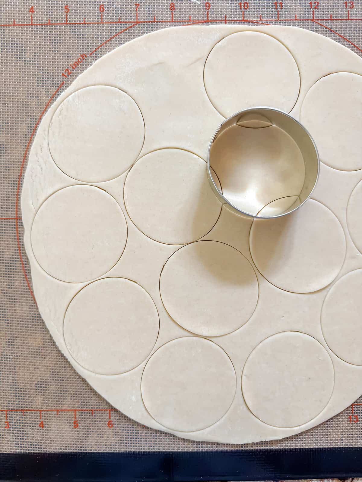 A metal biscuit cutter cuts circles from rolled-out dough on a silicone baking mat.