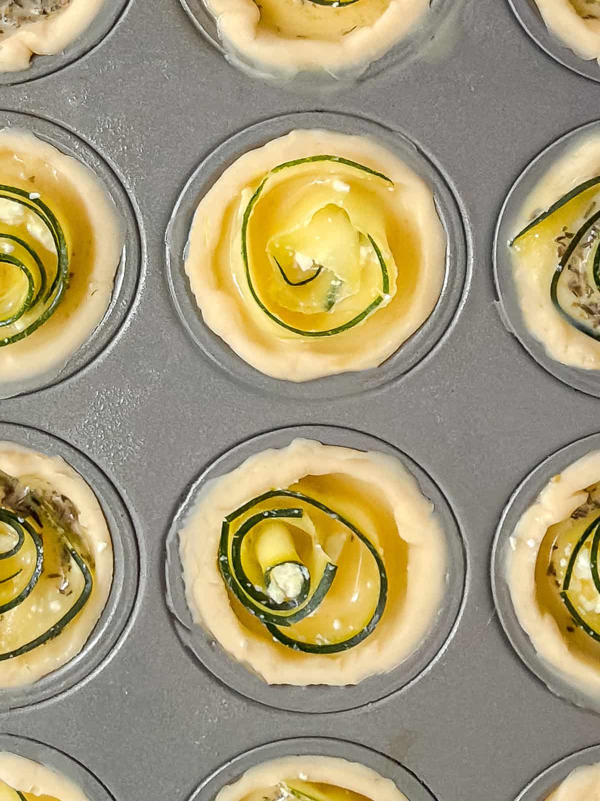 Close-up of a mini muffin tin filled with unbaked zucchini rose quiche appetizers.