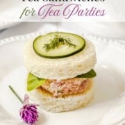 A round ham salad tea sandwich topped with cucumber and dill sits on a white plate, garnished with a purple flower. Text above reads, “Easy Ham Salad Tea Sandwiches for Tea Parties.” These elegant tea sandwiches are perfect for gatherings both big and small.