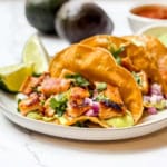 Three easy chicken tacos on a plate with lime wedges and avocados in the background.