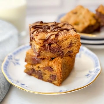Two chocolate chip cookie bars on a plate with a glass of milk in the background.
