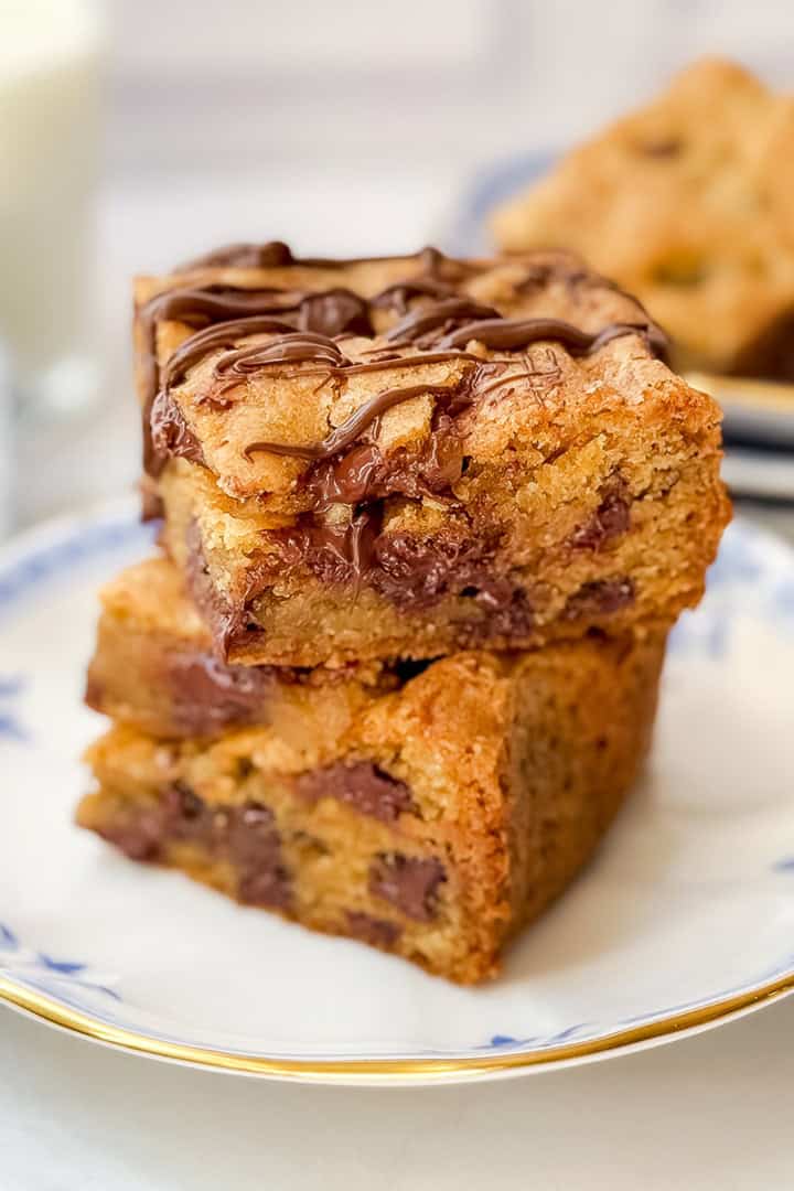 Two chocolate chip cookie bars on a plate with a glass of milk in the background.