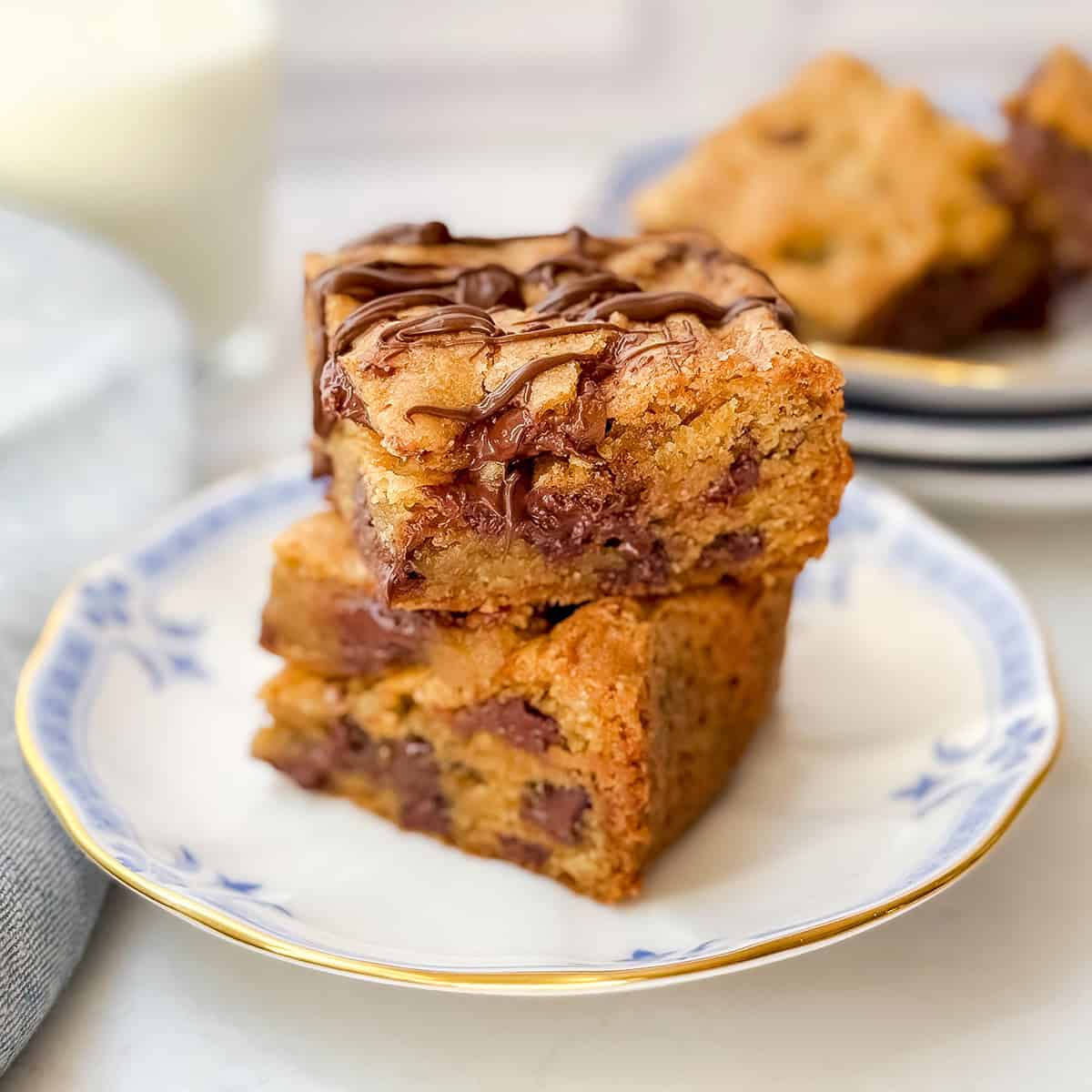 Two chocolate chip cookie bars on a plate with a glass of milk in the background.