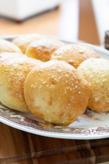 Golden homemade hamburger buns topped with coarse sea salt on a platter.
