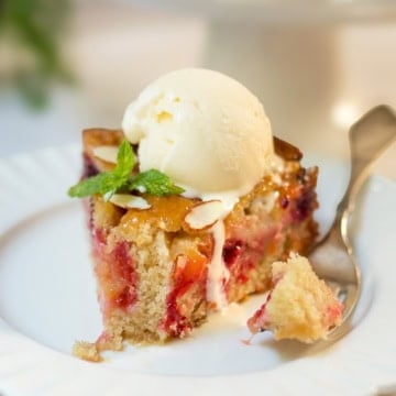 Slice of plum almond cake topped with vanilla ice cream and mint, showing fresh baked plums and a tender almond crumb with a fork nearby.