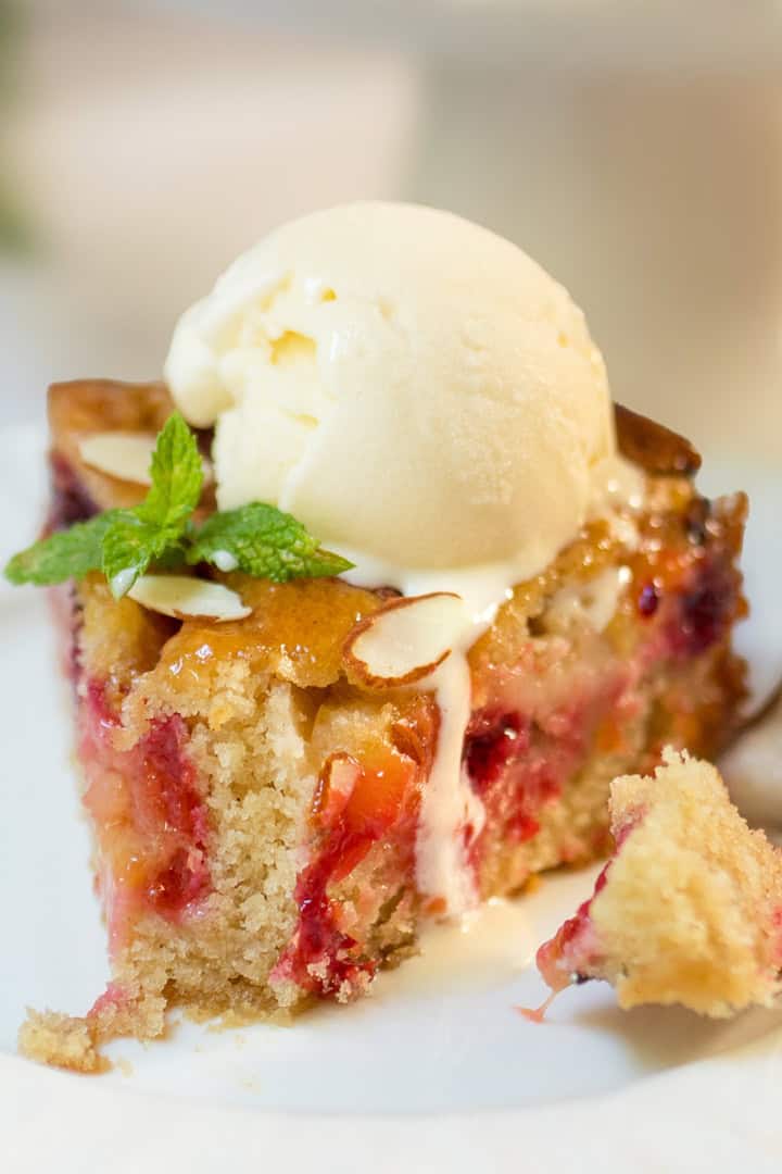 Slice of plum almond cake topped with vanilla ice cream and mint, showing fresh baked plums and a tender almond crumb with a fork nearby.