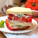 Closeup view of a tomato sandwhich with thickly sliced heirloom tomatoes, mayonnaise and basil leaves between two slices of sourdough bread.
