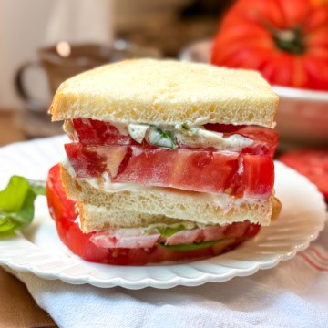 Closeup view of a tomato sandwhich with thickly sliced heirloom tomatoes, mayonnaise and basil leaves between two slices of sourdough bread.