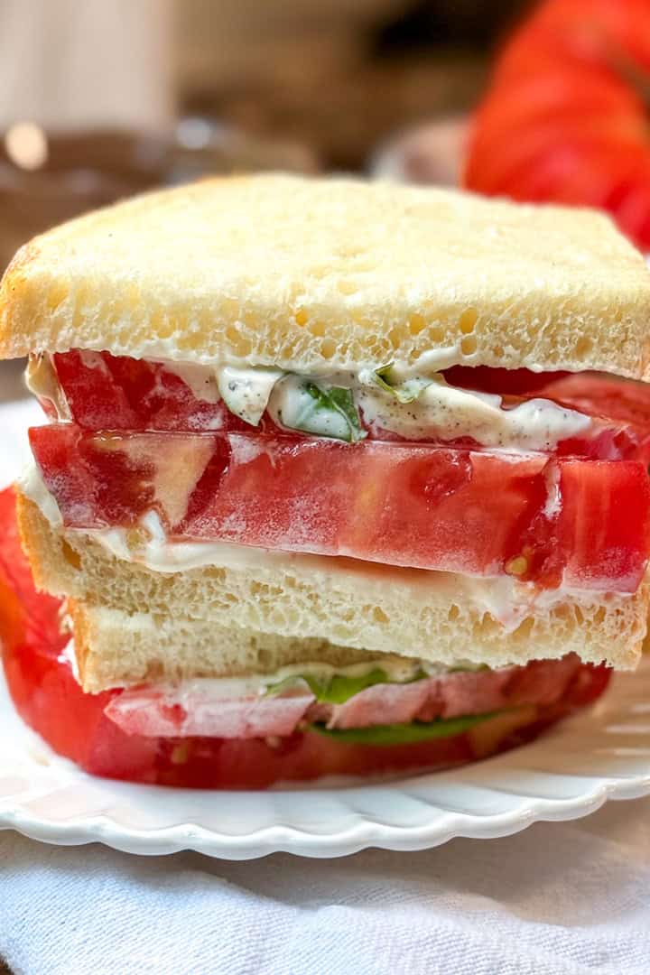 Closeup view of a tomato sandwhich with thickly sliced heirloom tomatoes, mayonnaise and basil leaves between two slices of sourdough bread.