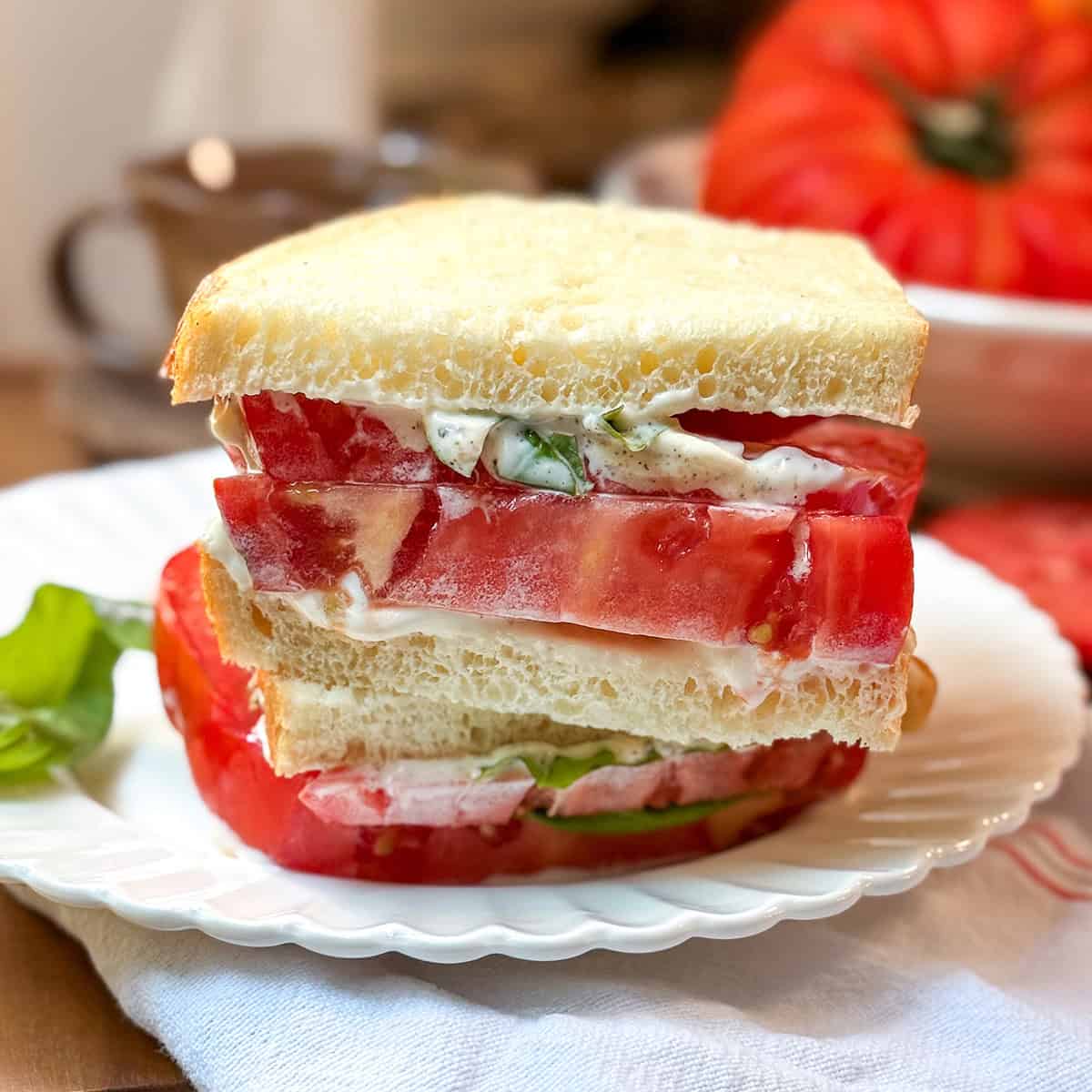Closeup view of a tomato sandwhich with thickly sliced heirloom tomatoes, mayonnaise and basil leaves between two slices of sourdough bread.