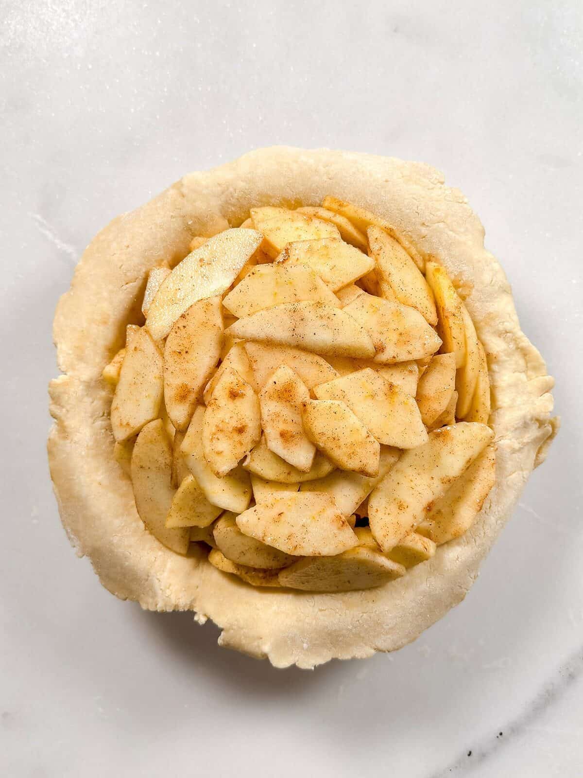Spiced sliced apples in a crust lined pie plate ready for the top crust.