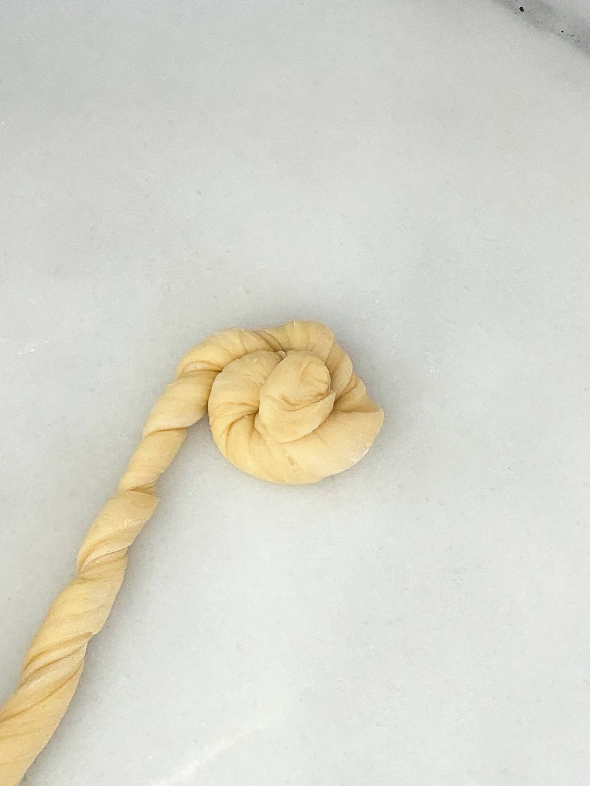A twisted piece of yeasted sweet dough is curled into a spiral shape on a white surface.