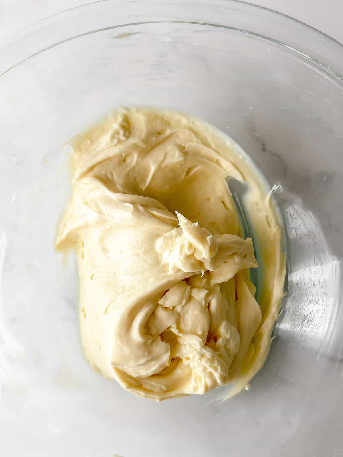 Thick, creamy yeasted sweet dough batter or frosting sits in a clear glass bowl on a white surface.