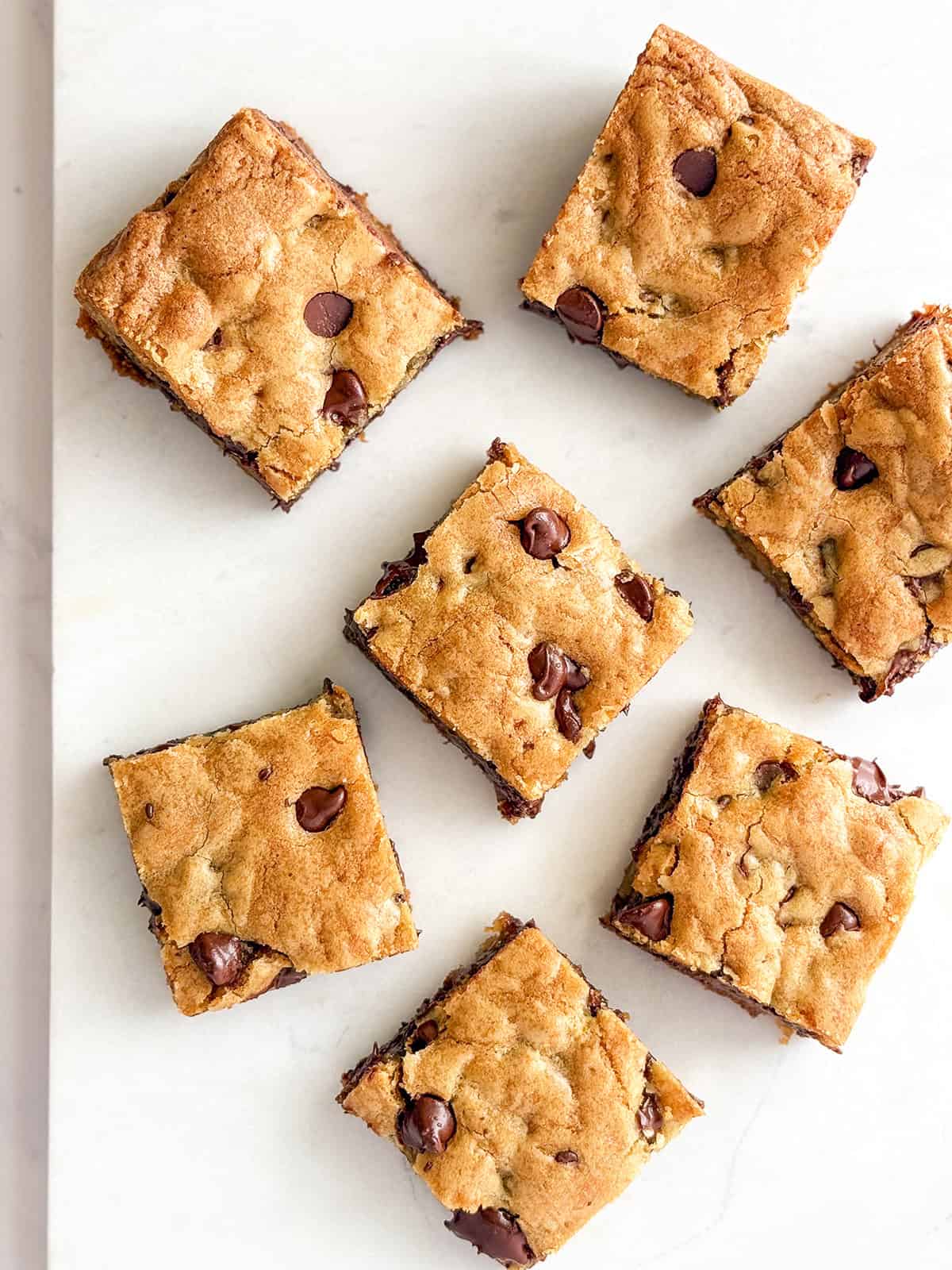 Top view of cut chocolate chip cookie bars on a white marble surface.