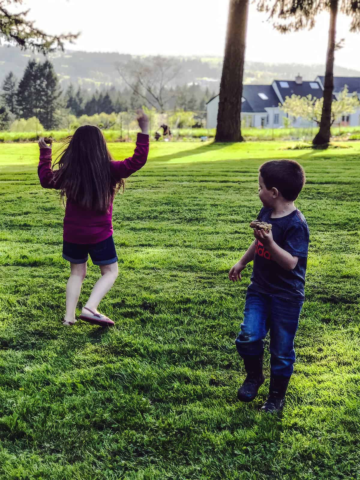 Two children playing in a summer backyard with chocolate chip cookie bars in their hands.