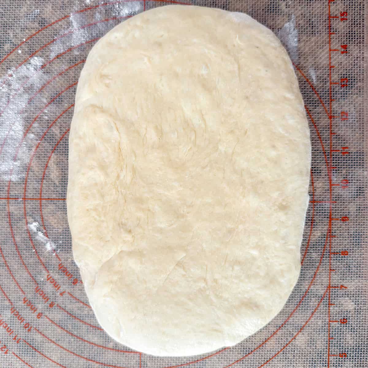 Hamburger bun dough patted into a rectangle on a floured work surface.