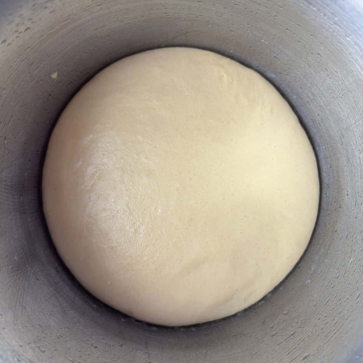 Hamburger bun dough resting in a stainless steel mixing bowl.