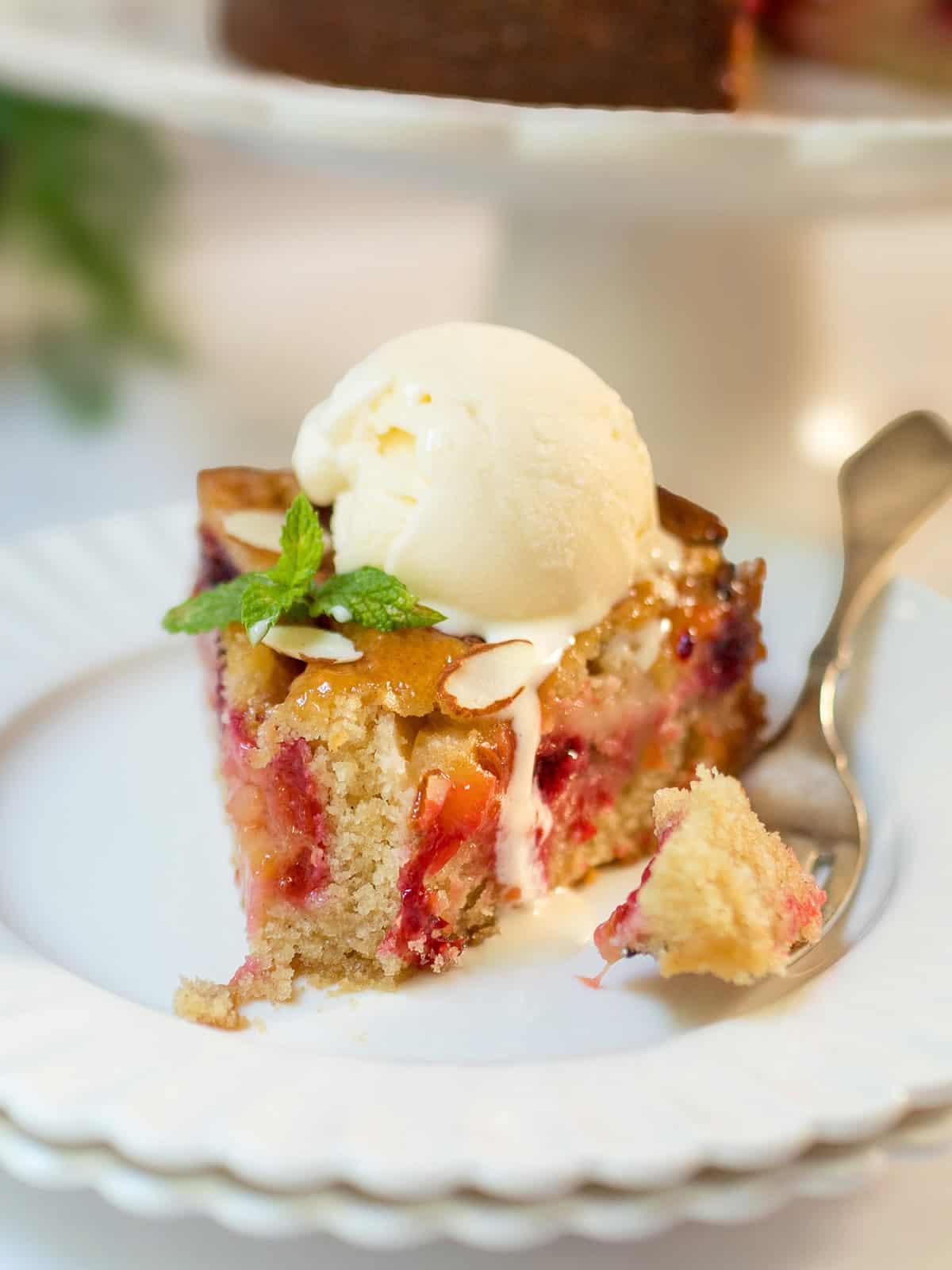 Slice of plum almond cake topped with vanilla ice cream and mint, showing fresh baked plums and a tender almond crumb.