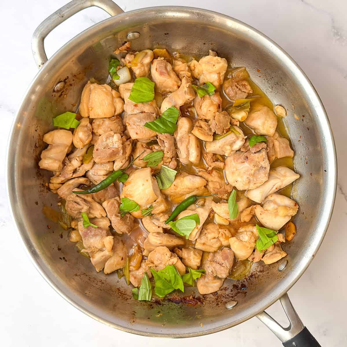 Three Cup Chicken simmering in a soy sauce and apple juice sauce until reduced and glossy.
