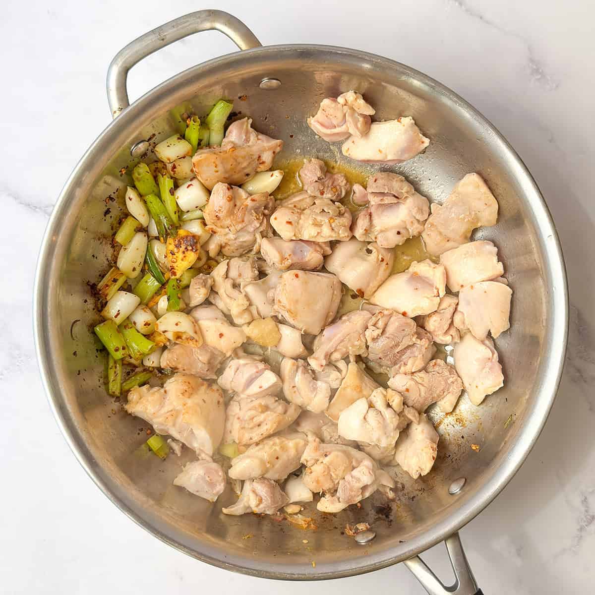 Bite-size pieces of chicken browning in a skillet with ginger, garlic, and scallions.
