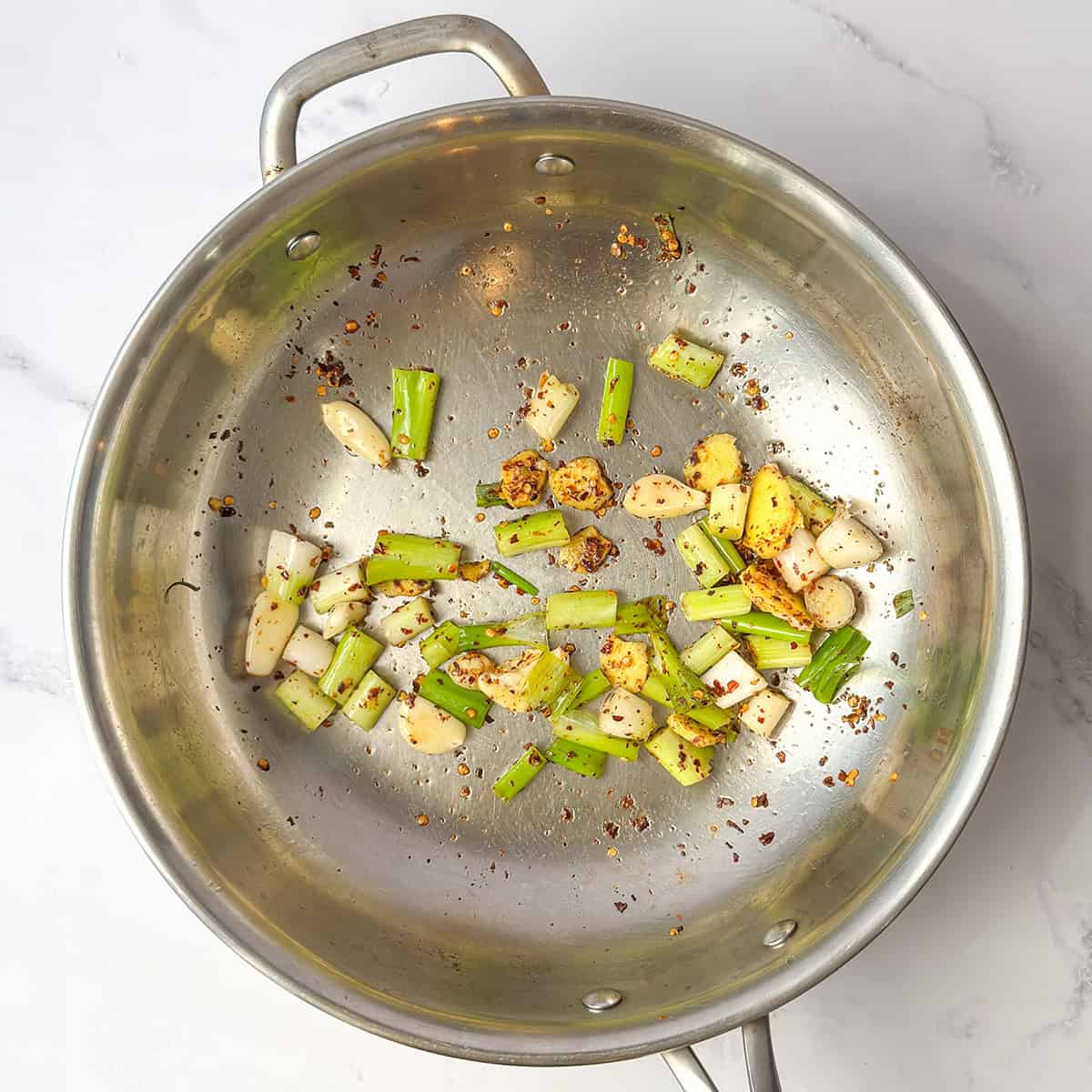Ginger, garlic, scallions, and red pepper flakes sautéing in sesame oil in a skillet.