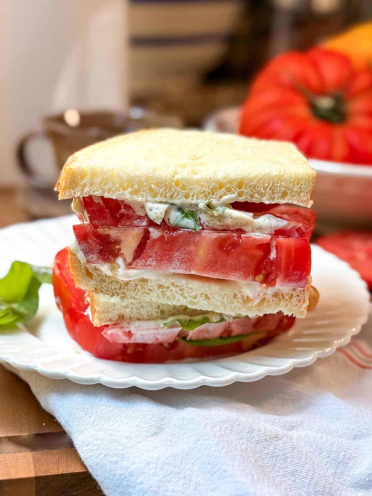Close-up of a tomato sandwich with thick heirloom tomato slices, mayonnaise, basil, and sourdough bread.