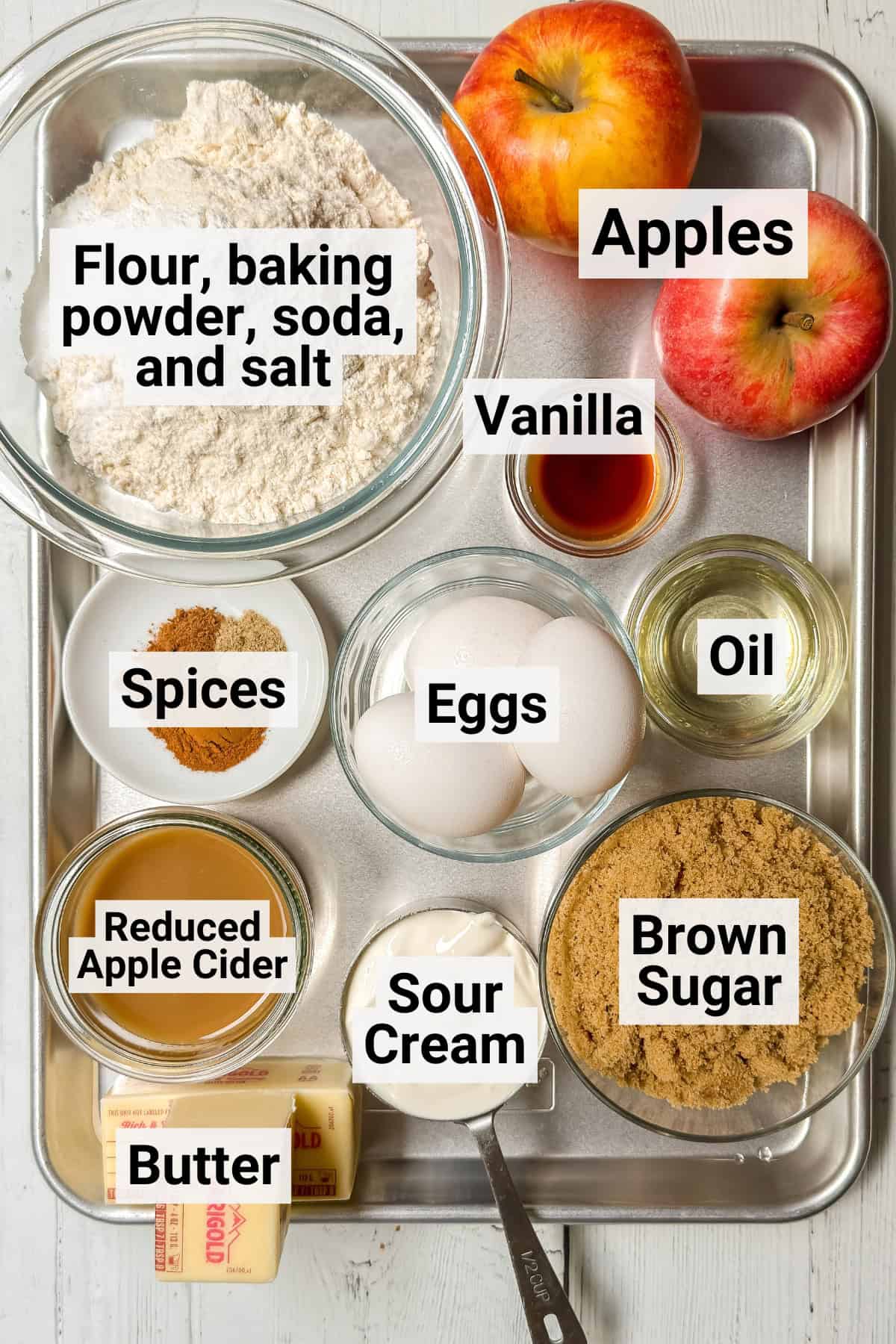 Labeled ingredients for apple cider Bundt cake, including apple cider, fresh apples, flour, brown sugar, butter, eggs, sour cream, vanilla, and warm spices.
