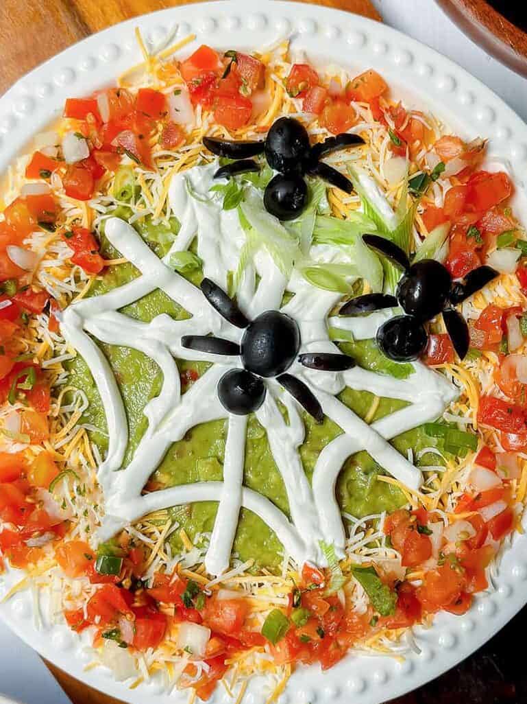 Halloween 7 Layer Dip topped with a sour cream spiderweb and black olive spiders.