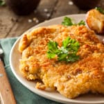 Chicken Schnitzel on a plate with roasted potatoes and garnished with fresh parsley.