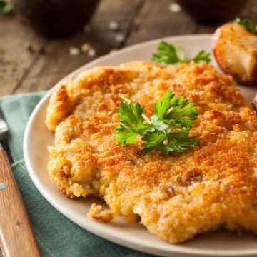 Chicken Schnitzel on a plate with roasted potatoes and garnished with fresh parsley.