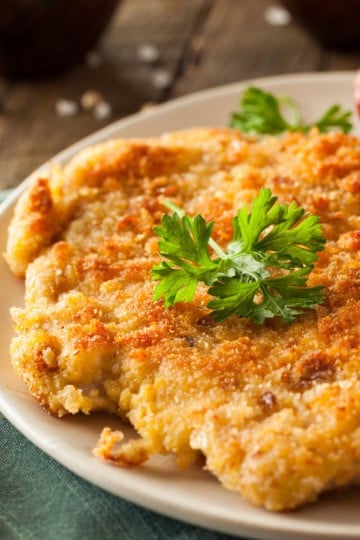 Chicken Schnitzel on a plate with roasted potatoes and garnished with fresh parsley.