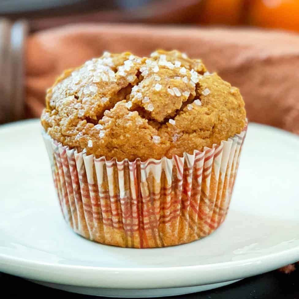 Square image of healthy pumpkin muffin in a fall paper sleeve resting on a small plate.