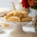 Ginger pear scones on a white pedestal stand with an autumn flower arrangement and teapot in the background.