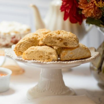 Ginger pear scones on a white pedestal stand with an autumn flower arrangement and teapot in the background.