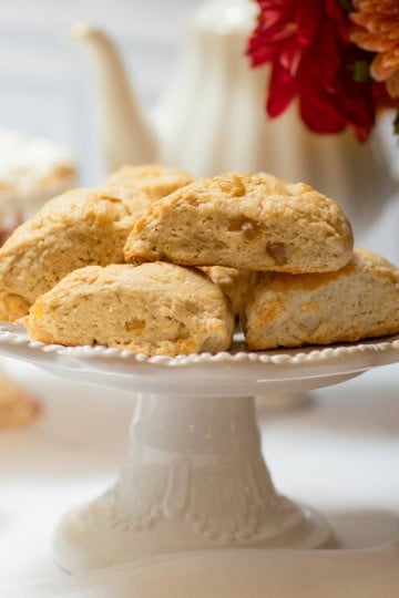 Ginger pear scones on a white pedestal stand with an autumn flower arrangement and teapot in the background.